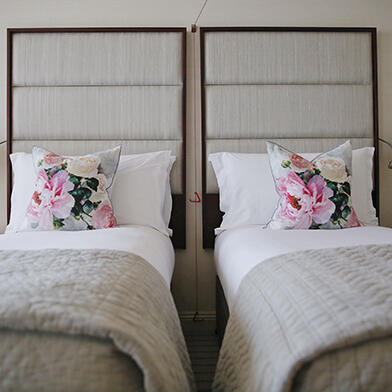 Two single beds with crisp white sheets and colorful pillows, neatly arranged in a classic room at the Westbury Hotel.