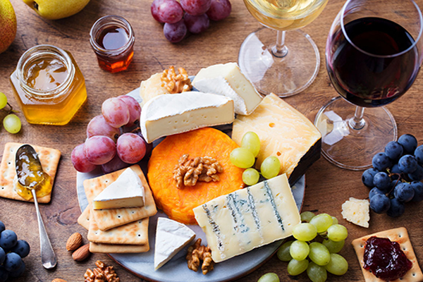 A gourmet cheese board with an assortment of cheeses, grapes, pears, crackers, jams, honey, and both red and white wine.