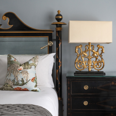 A twin room featuring a neatly made bed with white sheets and vibrant pillows, flanked by a dark black sideboard and complementary side lamp.