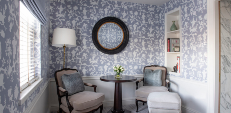Luxurious Studio Suite's sitting area featuring two elegant armchairs, a round central table with white tulips, and walls adorned with blue and white patterned wallpaper.